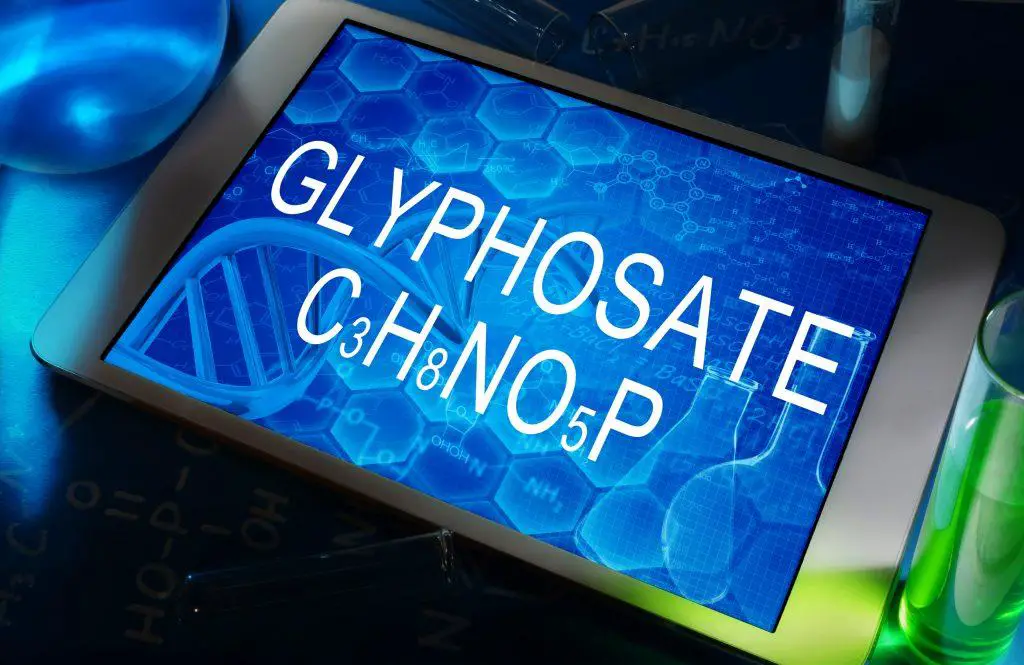 The chemical formula of glyphosate on a tablet with test tubes - glyphosate weed killer