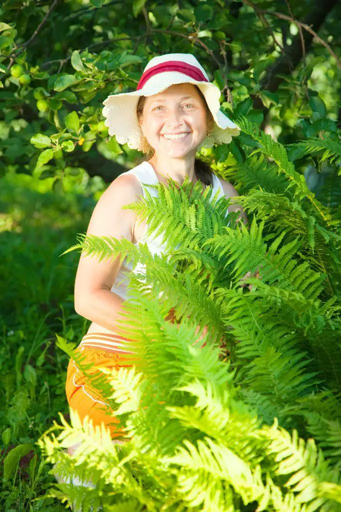 Woman in her backyard with a bush of ferns